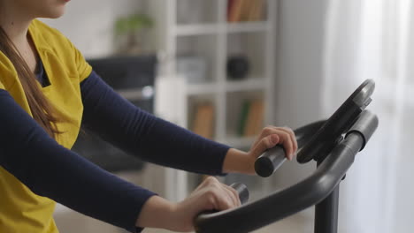 La-Mujer-Estudiante-Está-Entrenando-Con-Una-Bicicleta-Estática-En-La-Habitación,-Pedales-Giratorios,-Vista-De-Cerca-Del-Deporte-Y-El-Fitness-De-La-Cara-Y-El-Cuerpo-En-Casa